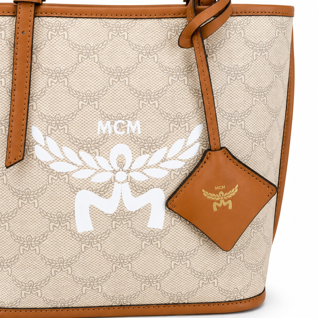 MCM beige laurel leaf with cognac-colored calfskin trim white logo and diamond pendant adjustable handle can be carried by hand over the shoulder or crossbody